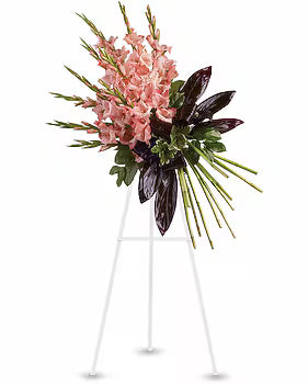 A floral arrangement featuring pink gladiolus flowers, dark burgundy leaves, and green foliage displayed on a white metal easel stand against a plain white background.