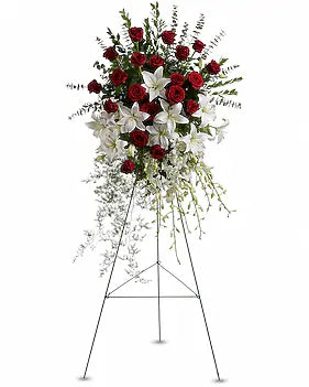 A large floral arrangement on a metal easel stand, featuring red roses, white lilies, and green foliage against a plain white background.