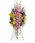 A large floral arrangement in a three-tier balloon style on a metal stand, featuring pink lilies, yellow daisies, purple flowers, and green foliage, isolated on a white background.